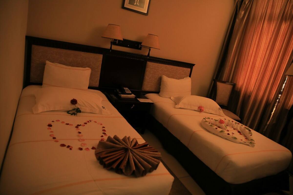 A hotel room with two beds, each with a heart-shaped arrangement of rose petals and a decorative pillow.