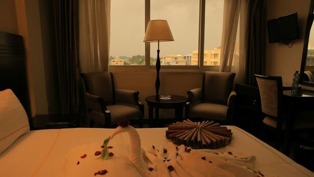 A hotel room with a bed, two armchairs, a small table, a lamp, and a TV on the wall. - Alwaq Hotel (Bahir Dar)