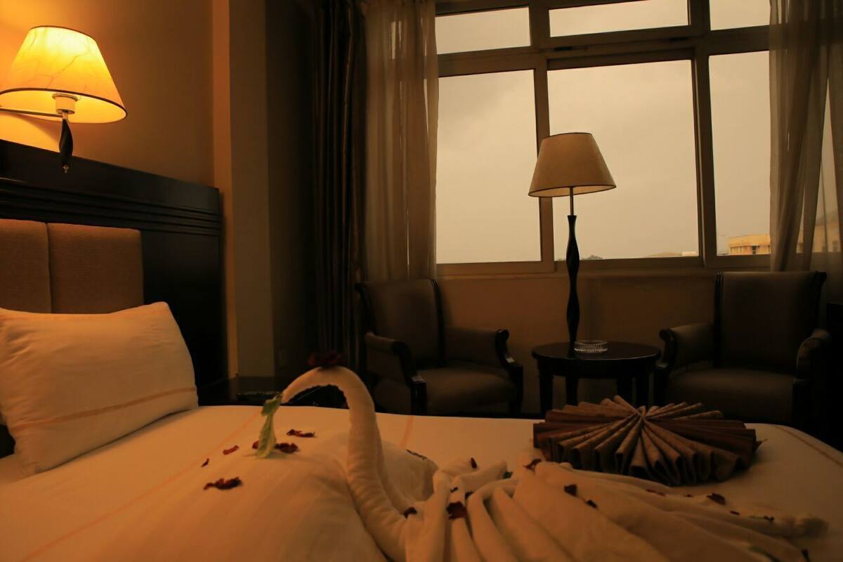 A hotel room with a bed, two chairs, a table, and a window with curtains.