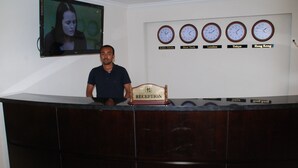 A reception desk with a television screen above it, displaying a woman. There are clocks on the wall indicating different time zones. - Alwaq Hotel (Bahir Dar)