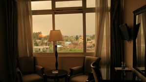 A room with two chairs, a small table, a lamp, and a large window with a view of buildings. - Alwaq Hotel (Bahir Dar)