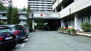 A parking lot with several cars, a building labeled "Apartment Haus" with a sign indicating "Kurhausstrasse 18", and a row of flower planters along the building's entrance. - Ferienwohnung Riefenbach (Bad Harzburg)