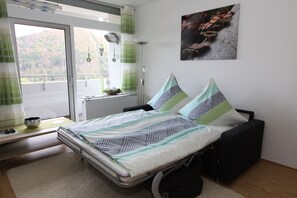 A bedroom with a bed, a window with curtains, a radiator, a wall-mounted picture, and a bedside table with a bowl. - Ferienwohnung Riefenbach (Bad Harzburg)