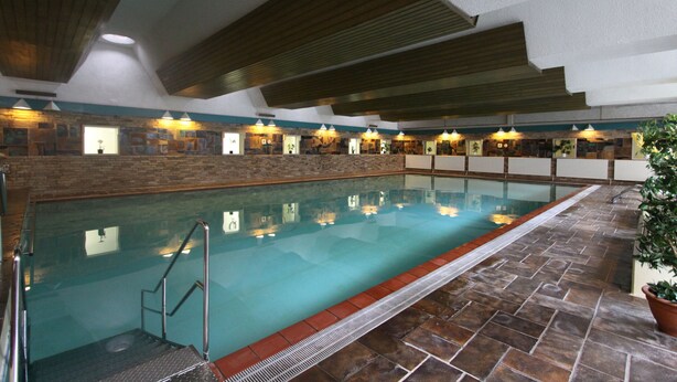 An indoor swimming pool with a stone wall, wooden ceiling beams, and a tiled floor. - Ferienwohnung Riefenbach (Bad Harzburg)