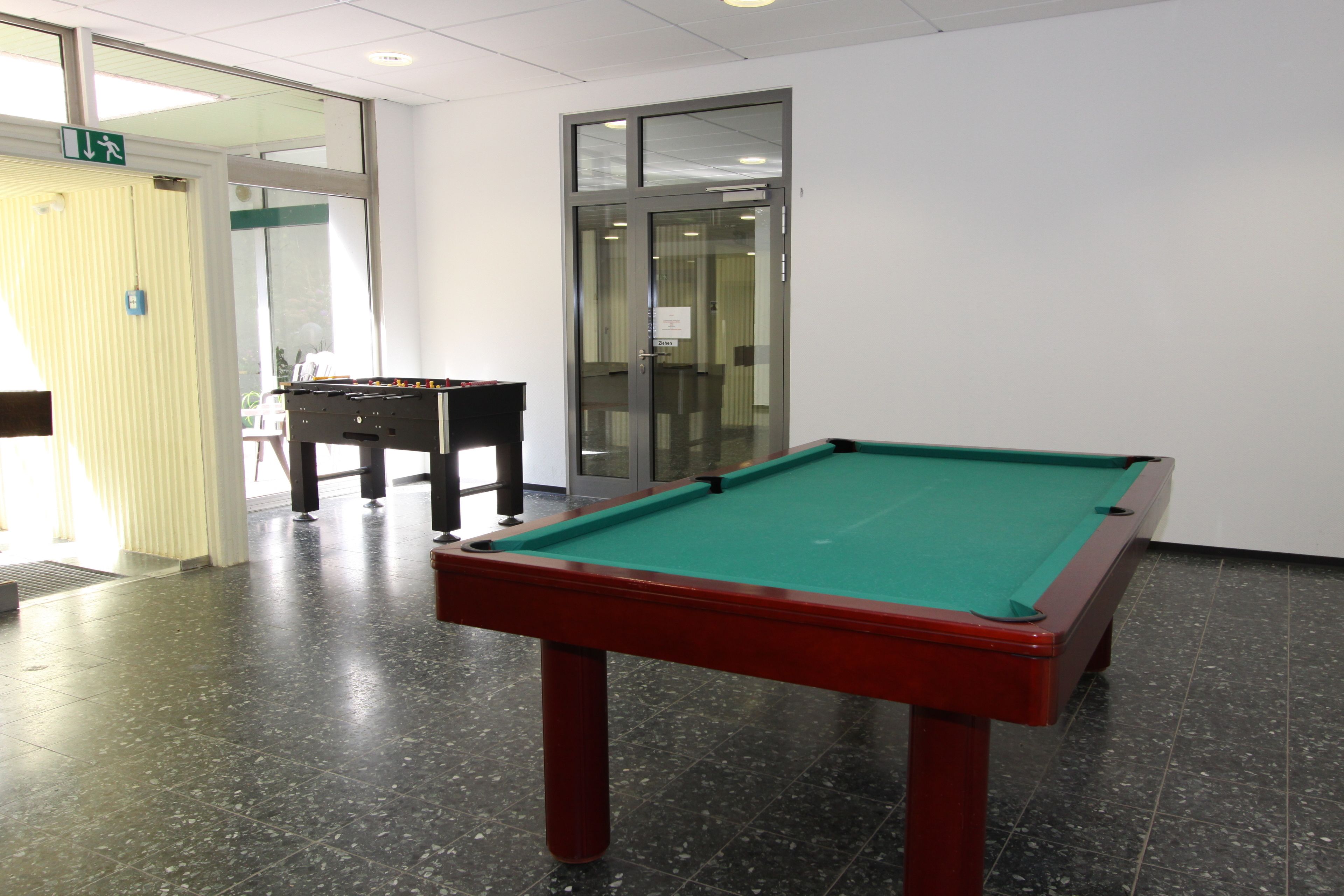 Mesa de bilhar em um ambiente com porta de vidro e uma cadeira.