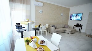 Una sala moderna con comedor, que incluye un sofá, sillas, un televisor y una mesa con alimentos para el desayuno.