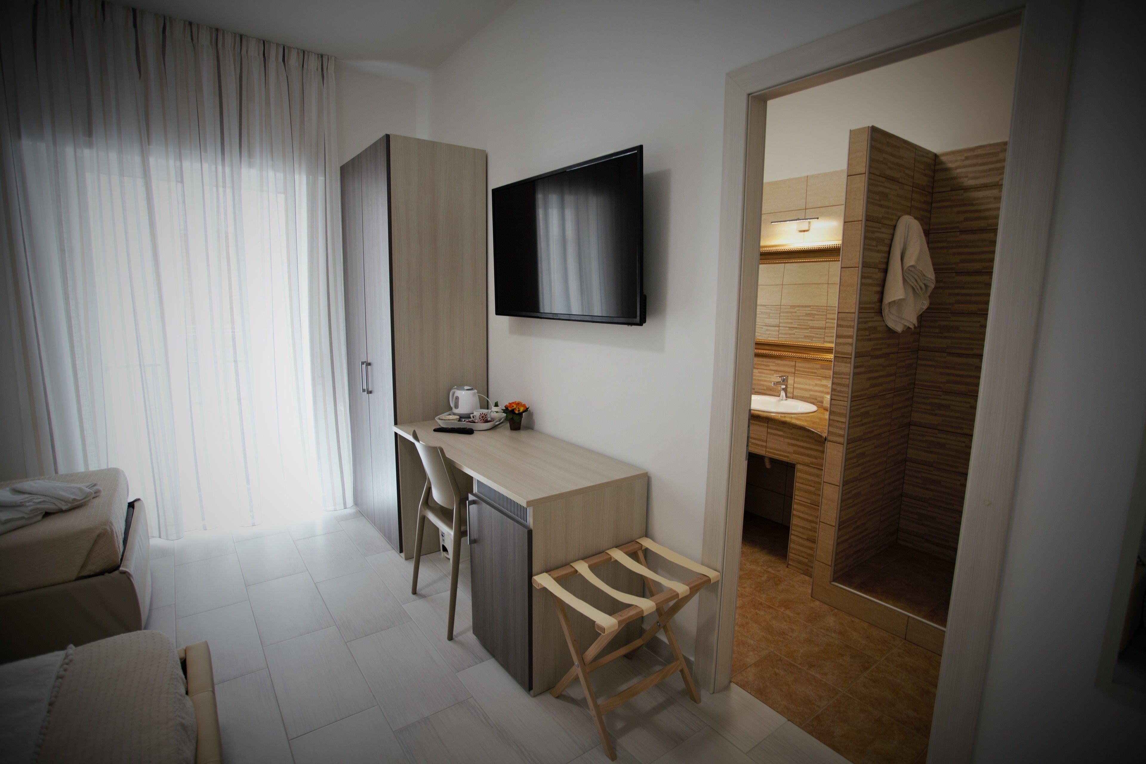 A modern hotel room with a desk, chair, TV, and a shower area.