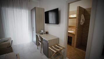 A modern hotel room with a desk, chair, TV, and a shower area.