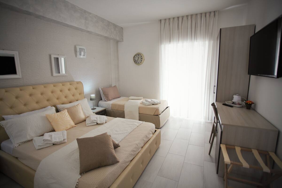 A hotel room with two beds, a desk, a chair, a TV, and a clock on the wall.