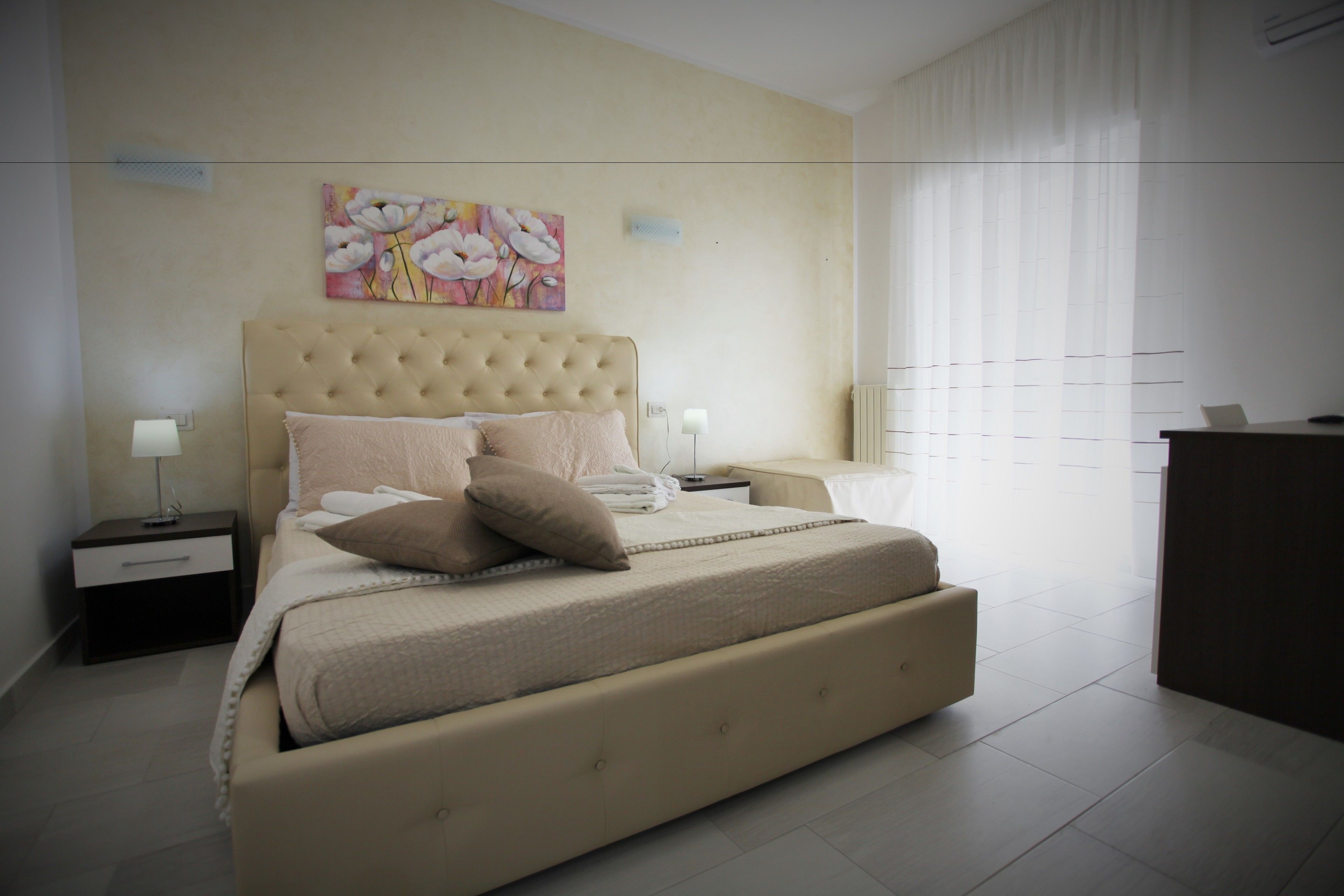 Une chambre à coucher avec un grand lit, deux tables de chevet, une commode, une coiffeuse et un tableau au mur.