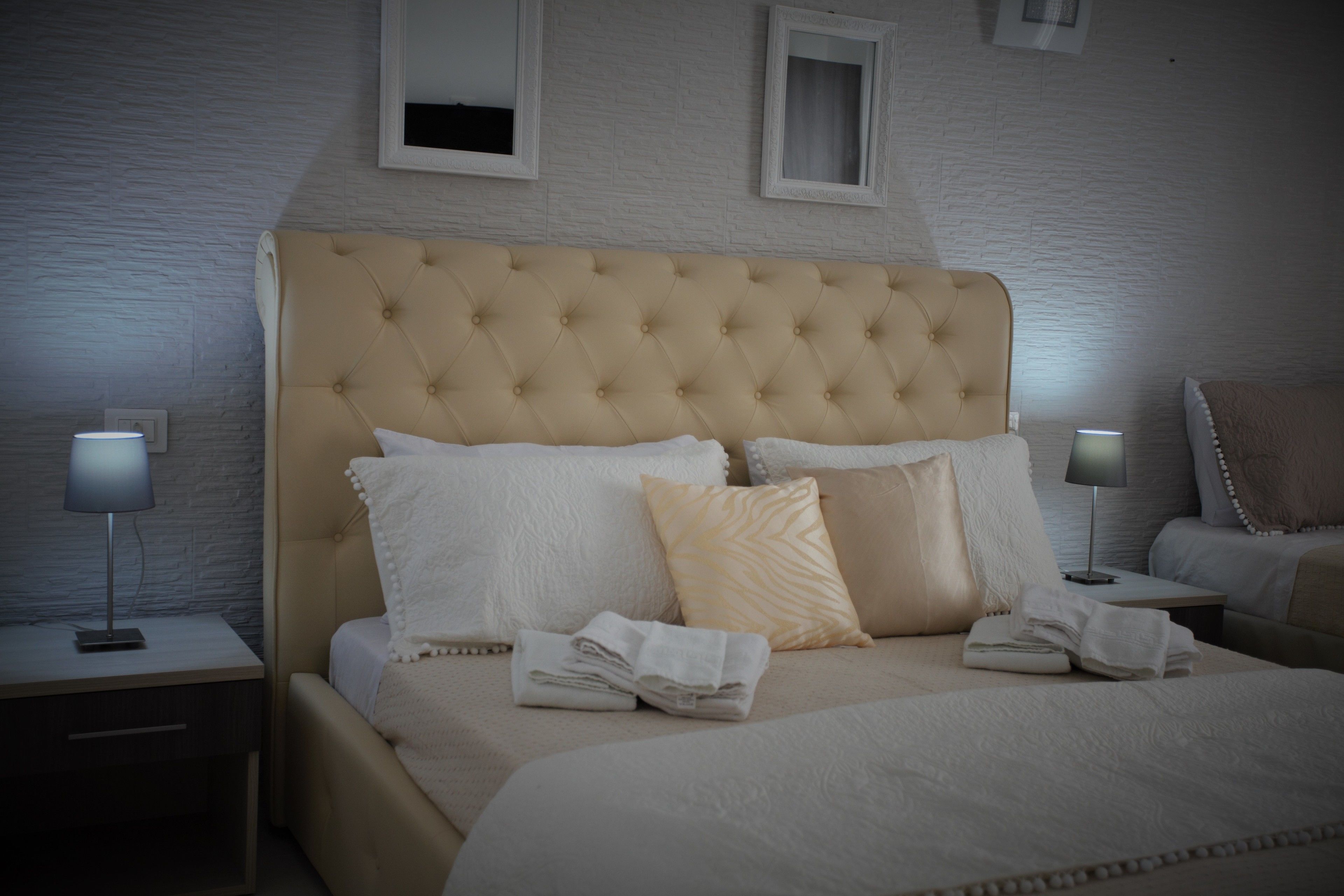 Un letto rifatto con cura, con una testiera imbottita, due comodini con lampade e una parete bianca con texture.
