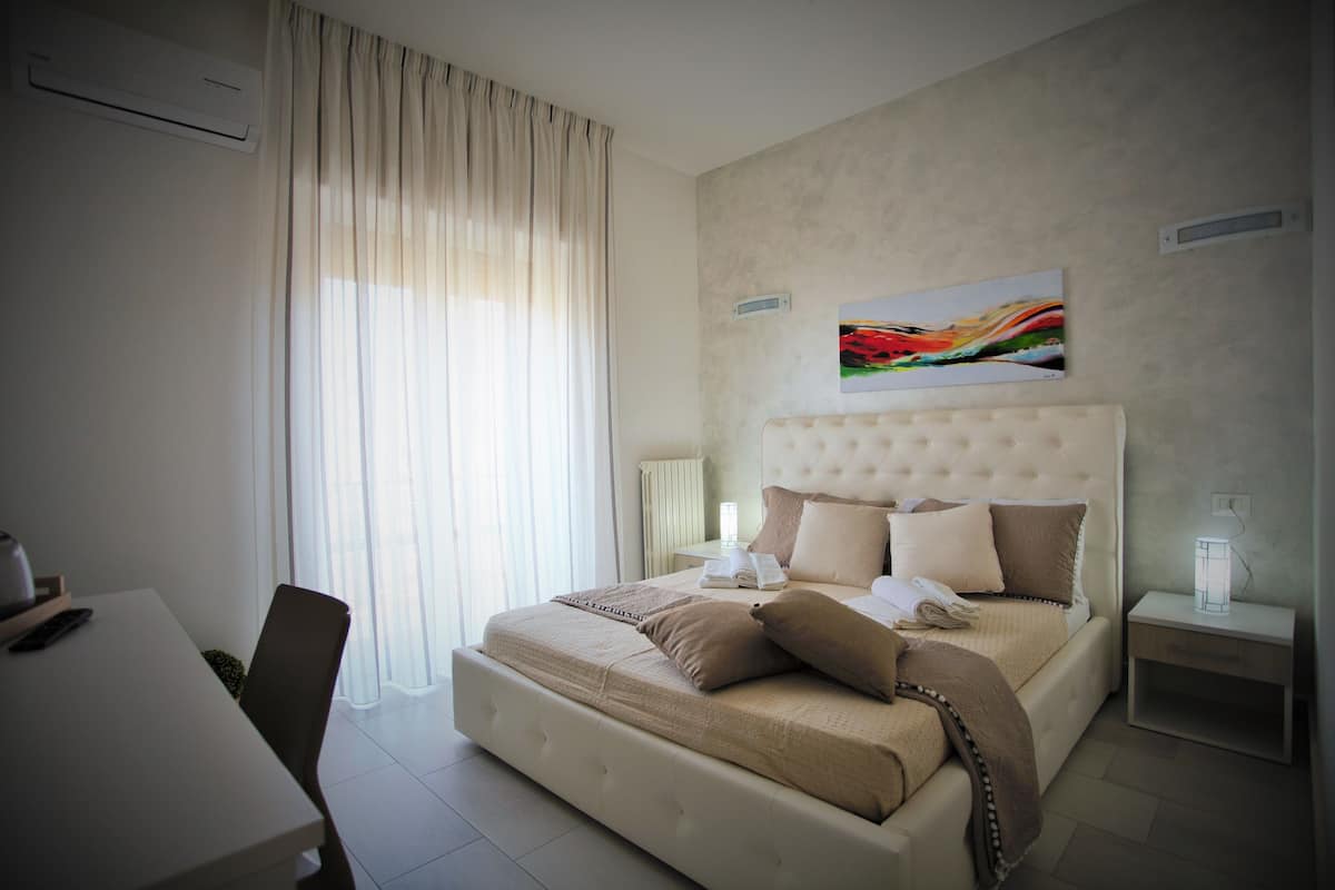 A modern bedroom with a large bed, a bedside table with a lamp, a chair, and a desk.