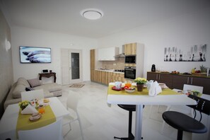 A modern kitchen with white cabinets, a microwave, and a stove. There is a dining area with a yellow tablecloth and chairs. - Central Apartments (Crotone)