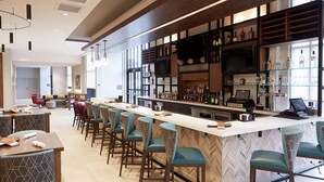 A bar area with a long counter, multiple stools, and a variety of bottles and glasses on shelves. - Hilton Garden Inn Elizabethtown, KY (Elizabethtown)