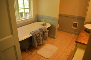 A bathroom with a bathtub, a window, a wooden floor, and a white rug.