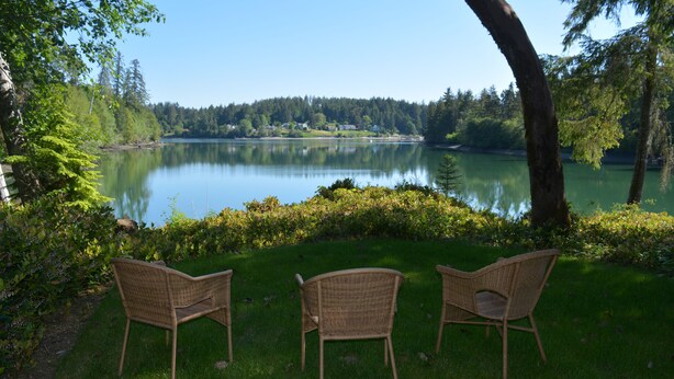 A view of a lake with two wicker chairs facing the water, surrounded by greenery and trees. - Two Herons Cottage (Shelton)