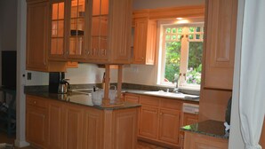 A kitchen with wooden cabinets, granite countertops, and a window with a view of greenery. - Two Herons Cottage (Shelton)