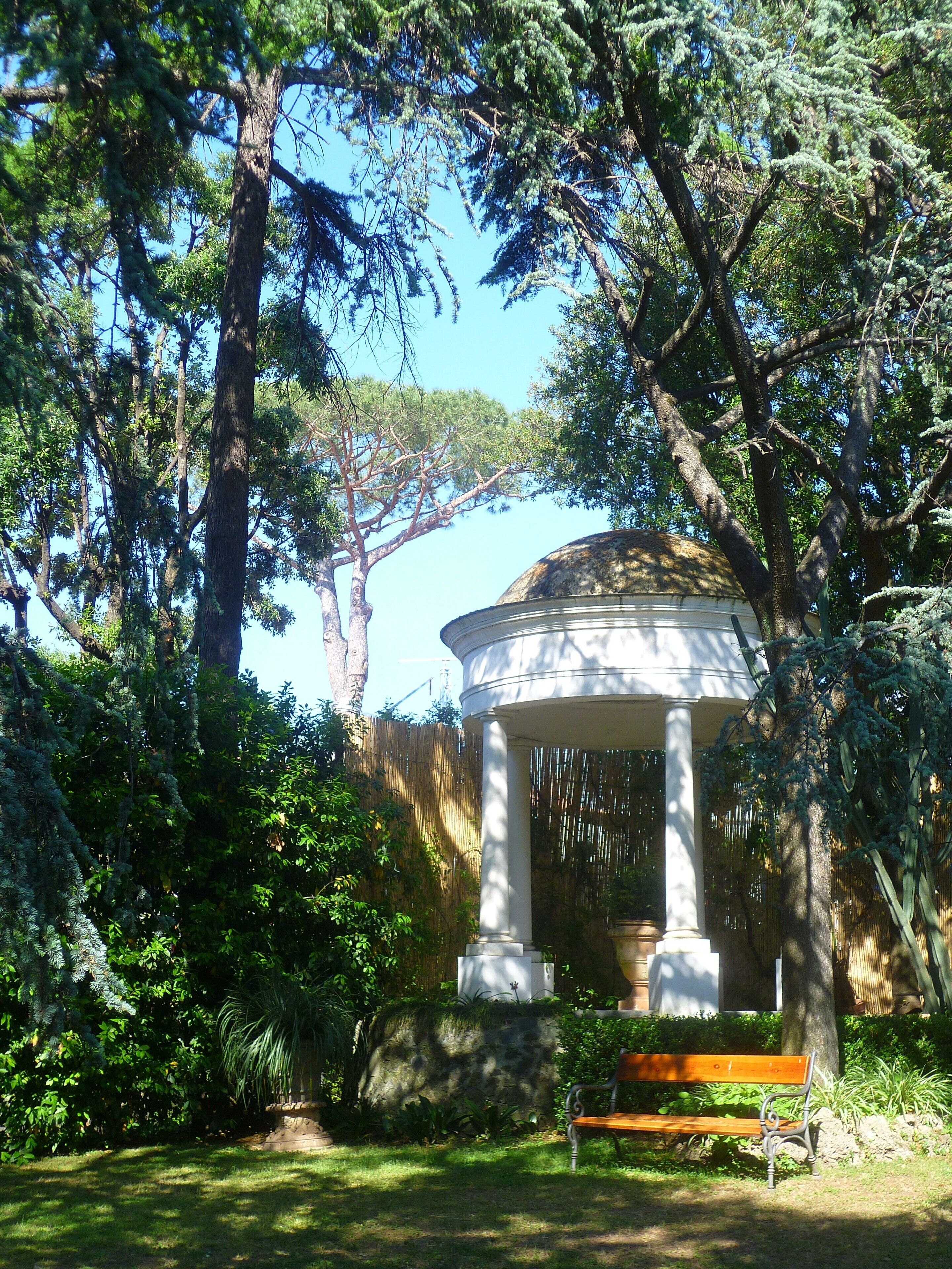 A gazebo with a dome roof surrounded by lush greenery and trees.