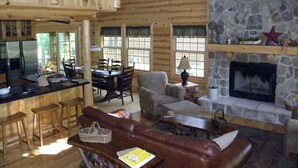 Un intérieur de chalet chaleureux avec une cheminée en pierre, un coin repas en bois et un espace salon confortable.