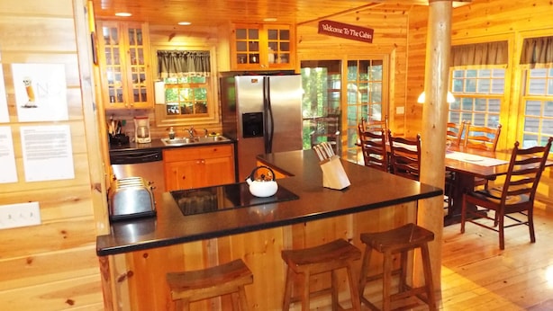 Une cuisine de style rustique, avec des éléments en bois, comprenant un îlot central, des tabourets de bar et un coin repas avec des chaises en bois.