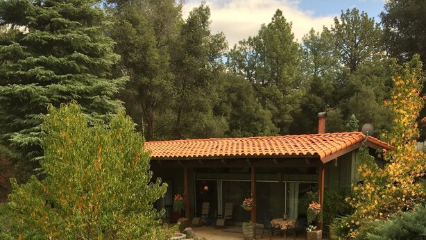 Une maison avec un toit en tuiles, entourée d’une végétation luxuriante et d’arbres.