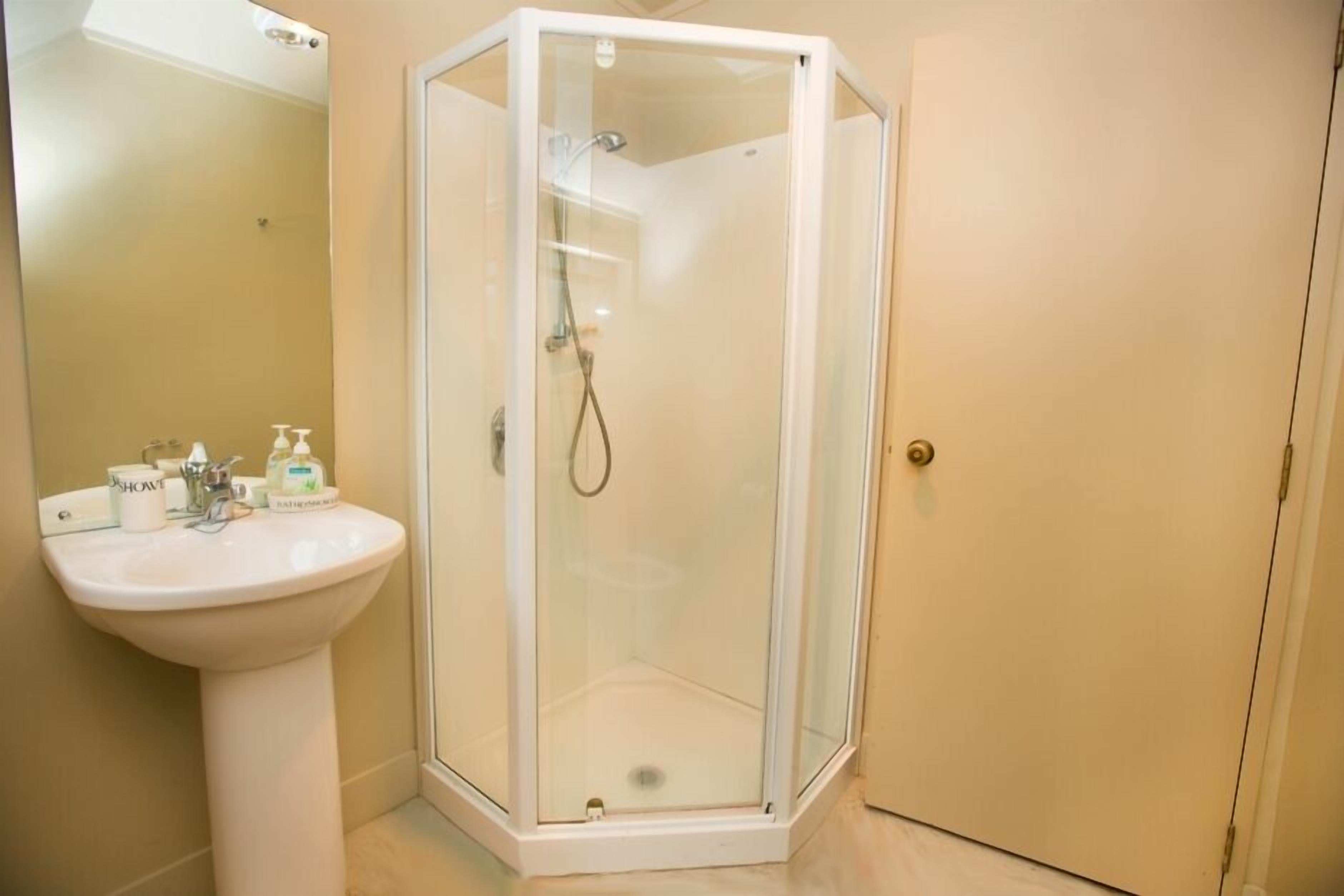 A bathroom with a glass-enclosed shower, a pedestal sink, and toiletries on the sink.