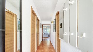 A hallway with wooden doors and white walls, leading to a room with a bed and a window. - RUBENS C1 Almadrava (Rosas / Roses)