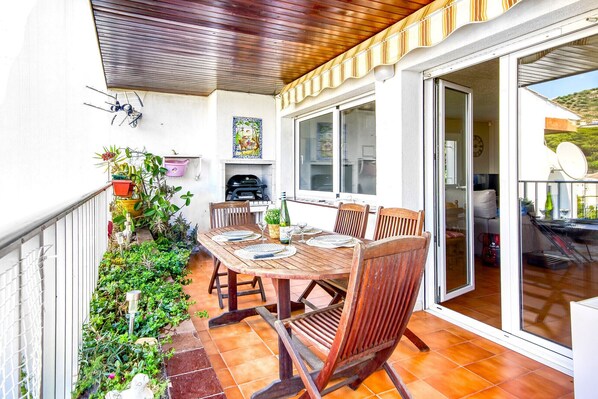 A patio with a wooden table and chairs, surrounded by potted plants and a grill. - RUBENS C1 Almadrava (Rosas / Roses)