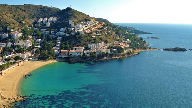 A coastal town with buildings on a hillside overlooking a clear blue sea. - RUBENS C1 Almadrava (Rosas / Roses)