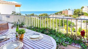 A balcony with a wooden table set for dining, overlooking a coastal view with buildings and greenery. - RUBENS C1 Almadrava (Rosas / Roses)