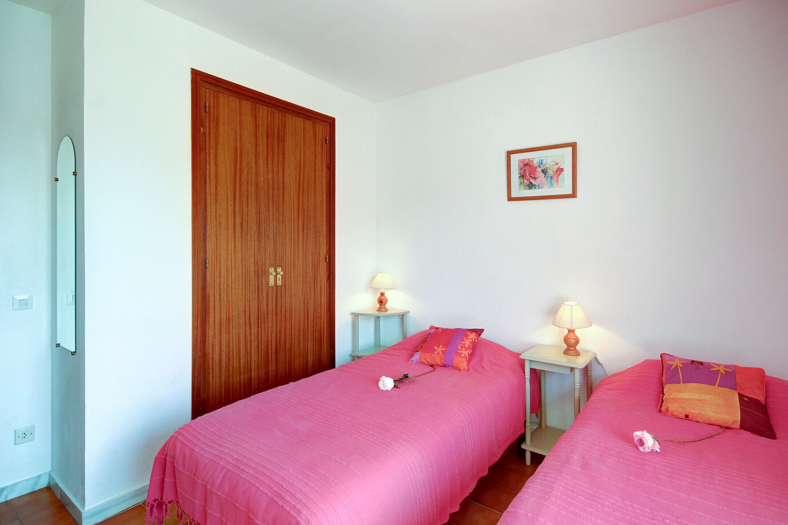 Une chambre avec deux lits, une porte en bois, une petite table avec une lampe et un tableau encadré au mur.