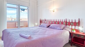 Quarto com uma cama grande, cabeceira vermelha, mesa de cabeceira com abajur e janela com cortinas.