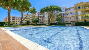 Piscina com bordas azulejadas, rodeada por edifícios com várias andares, varandas, árvores e áreas de estar ao ar livre.