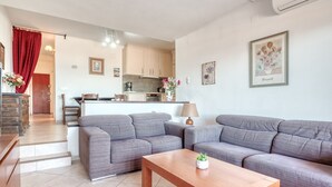 Uma sala de estar moderna com dois sofás cinzentos, uma mesa de centro de madeira e uma cozinha ao fundo.