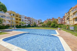 Une piscine entourée d’immeubles à plusieurs étages dotés de balcons, un ciel dégagé et un panneau indiquant les équipements disponibles au bord de la piscine.