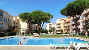 A swimming pool surrounded by apartment buildings, with trees and lounge chairs.