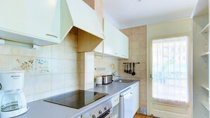 Una cocina moderna con estufa, horno y lavavajillas integrados, además de cafetera y ventana con cortinas.