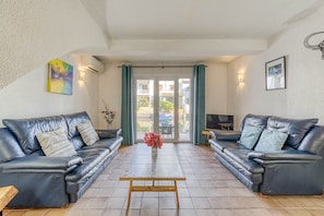 A living room with two leather sofas, a coffee table, and a view through a glass door to an outdoor area with boats. - ISLA CARTAGO 49 Empuriabrava (Empuriabrava)