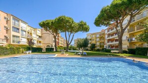 A swimming pool with lounge chairs, surrounded by multi-story buildings with balconies and trees.