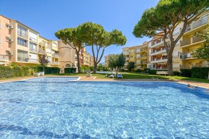A swimming pool with lounge chairs, surrounded by multi-story buildings with balconies and trees.