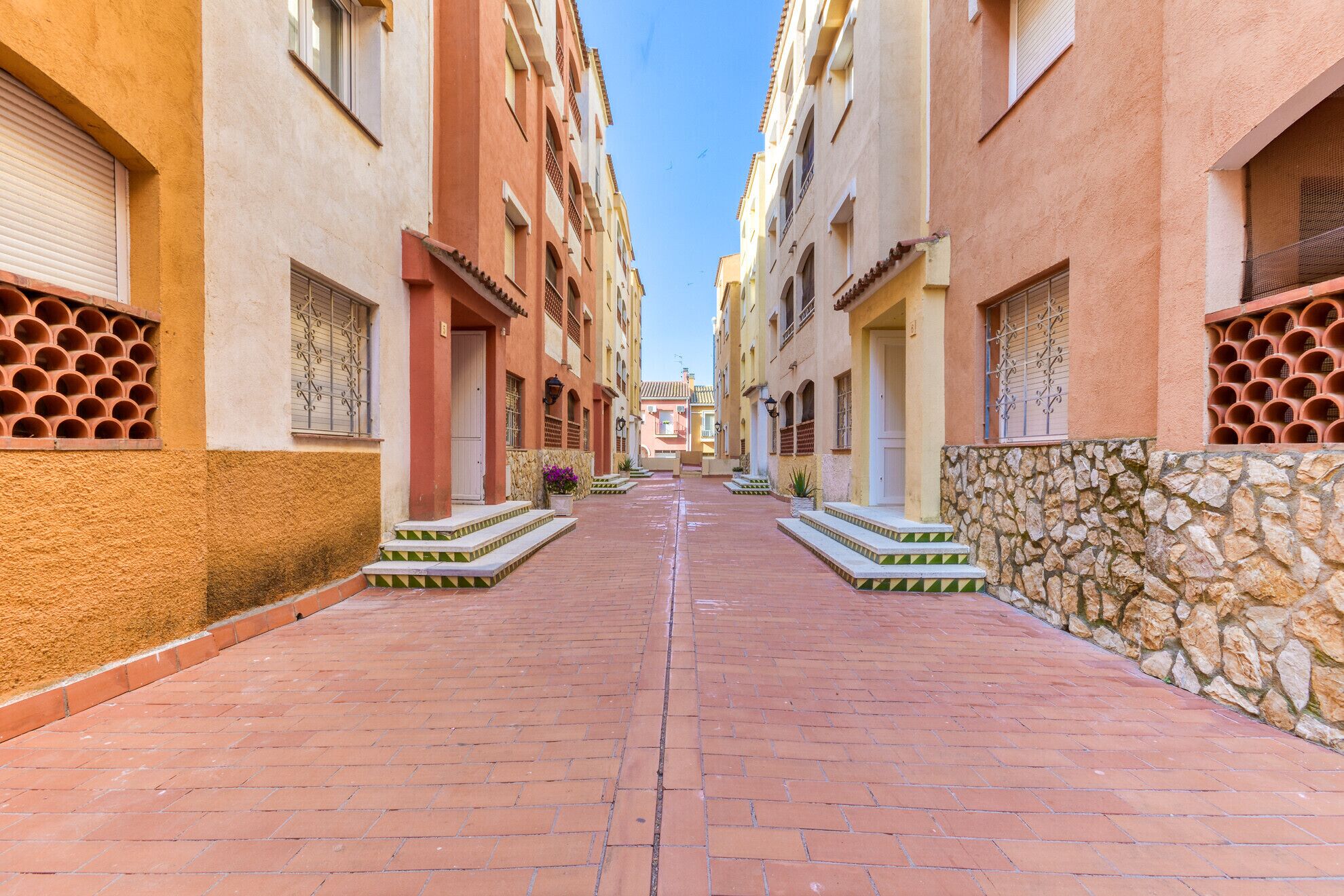 A narrow street with buildings on either side, featuring a central pathway and stone walls.