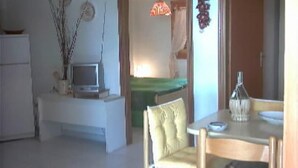 Una sala de estar con comedor, un televisor sobre un mueble bajo, una mesa con sillas y una lámpara colgante.