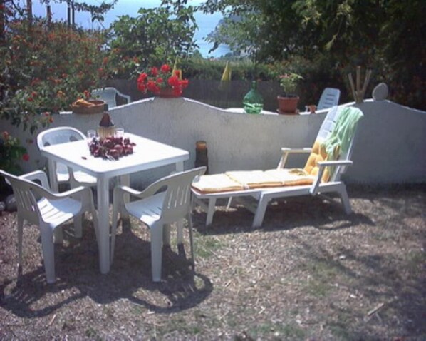 Un patio con una mesa y sillas, una silla de descanso y plantas en macetas.