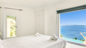 A bedroom with a large window, a bed, a towel, and a door. - VILLA LOU Roses (Rosas / Roses)