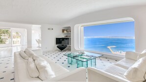 A modern living room with a glass coffee table, white sofas, and a large window with a view of the sea. - VILLA LOU Roses (Rosas / Roses)