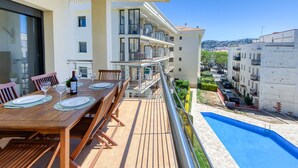 A balcony with a wooden table set for dining, overlooking a swimming pool and a residential area.