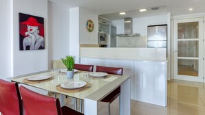 A modern kitchen with stainless steel appliances, a dining area with red chairs, and a glass table. - MILENI 1 1 4 3 Roses (Rosas / Roses)