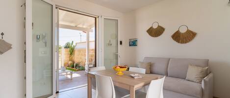 Una sala de estar moderna con un sofá, una mesa de comedor con sillas y un ventanal que da a un espacio al aire libre.