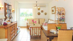 A cozy living room with a sofa, dining table, wicker chairs, a bookshelf, and a chandelier. - PORT SOTAVENT 2A (Empuriabrava)