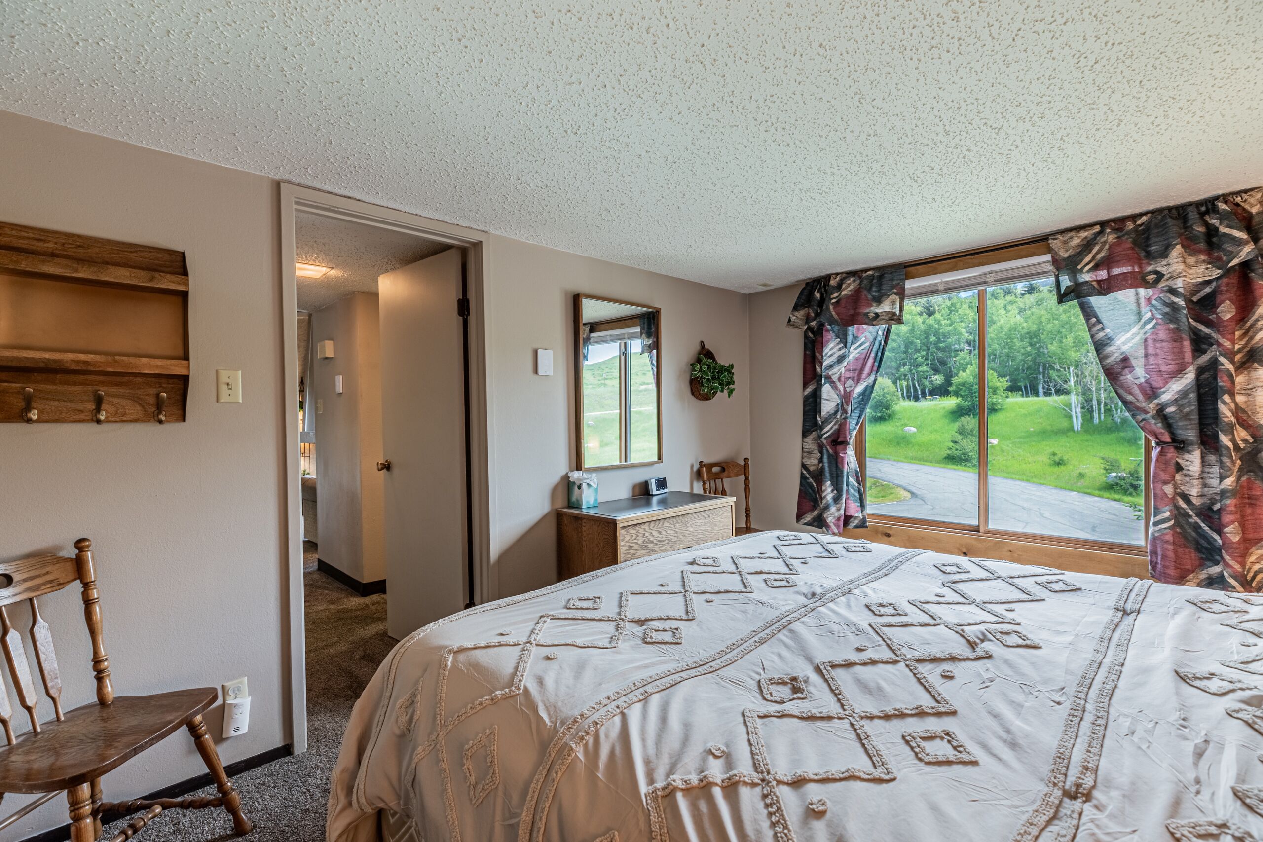A bedroom with a large bed, a wooden chair, a desk, and a window with curtains.